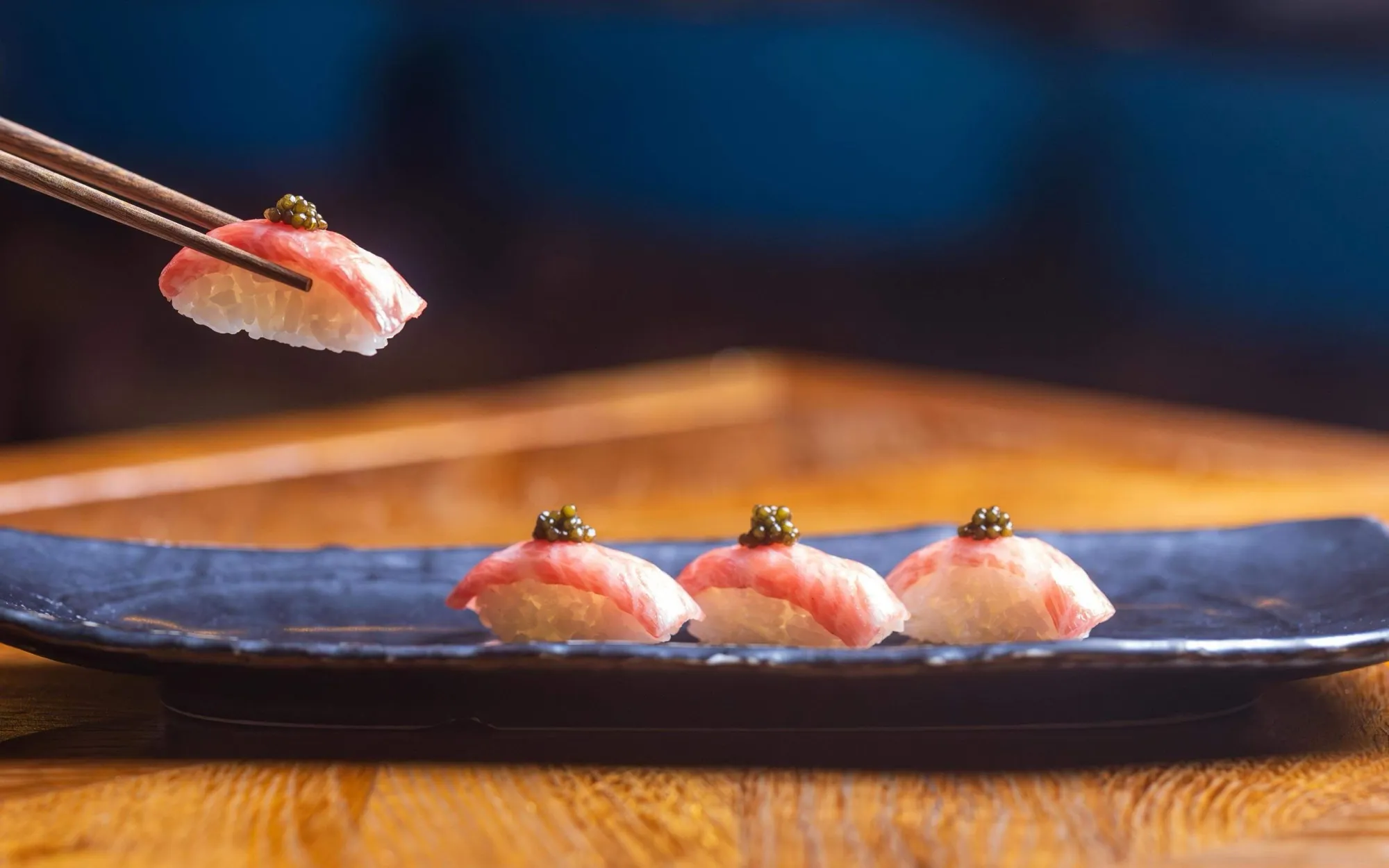 Nigiri lifted with chopsticks over a wooden counter